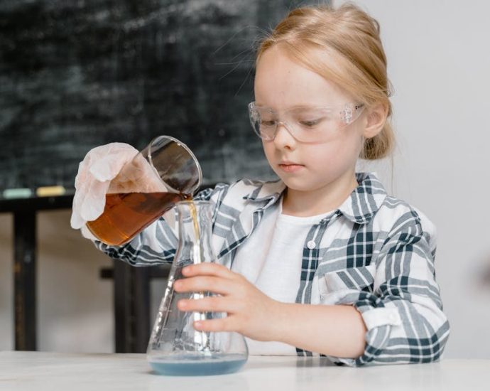 A young girl in safety goggles pouring liquid in a classroom science experiment.