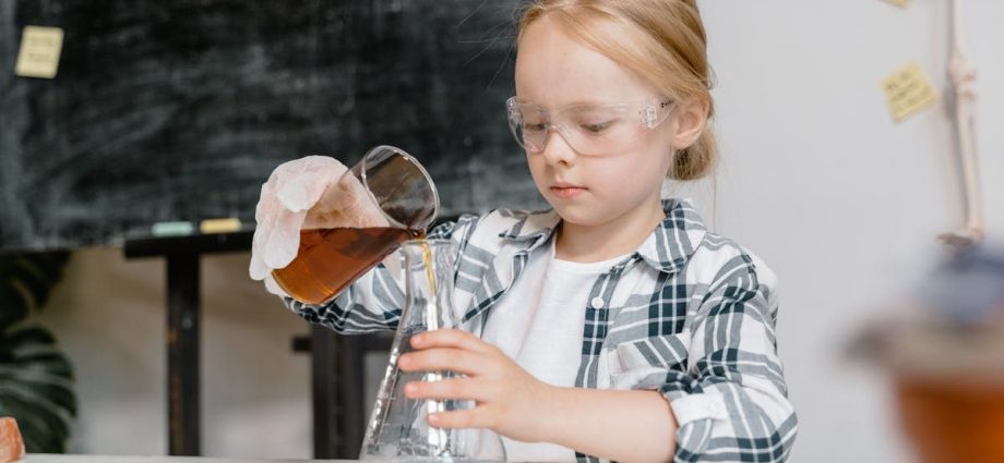 A young girl in safety goggles pouring liquid in a classroom science experiment.